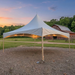 20x20 High Peak Frame Party Tent with string lights set up on a gravel driveway near a red barn at sunset.