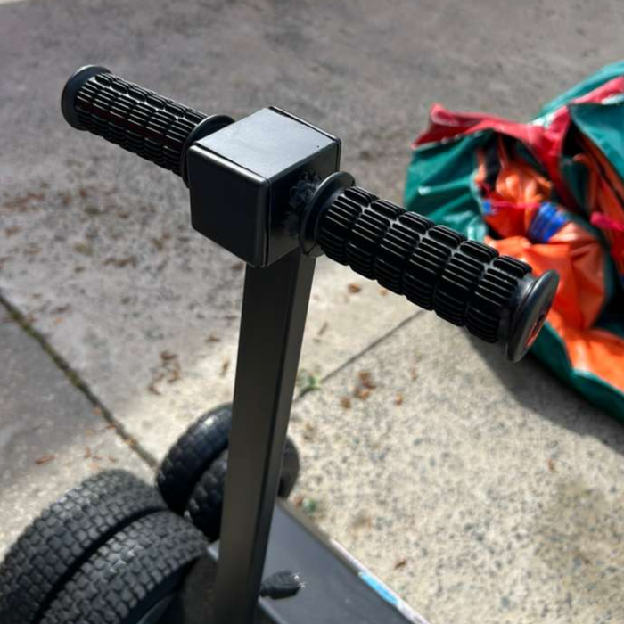 Close-up of the IRM-2000 inflatable roller machine's textured rubber grip handlebars and steel control frame, shown next to a rolled commercial PVC inflatable on a sunny outdoor surface