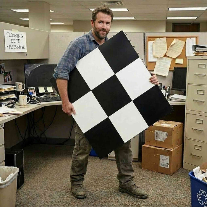 Man holding a large checkered floor tile in an office setting
