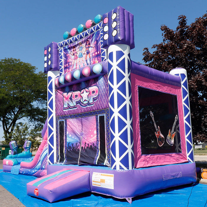 Close-up front angle of the KPOP Combo Wet N Dry showing the KPOP center display panel with concert stage graphics, colorful disco light orbs across the top arch, silver chrome truss framing on both sides, finger-proof mesh safety netting window on the right side of the bounce chamber, and a blue inflatable splash pool at the base. Trees and blue sky in background.