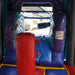 Game Over Wet & Dry Bounce House Combo with Slide, interior entrance view with purple and teal galaxy-themed graphics, a black rolled overhead bolster obstacle, a red punch obstacle pillar, and a safety rules sign panel, with a parked van visible through the mesh window