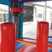Game Over Wet & Dry Bounce House Combo with Slide, interior view showing red padded obstacle pillars and mesh netting inside the play area, with a manufacturing warehouse visible through the open mesh window in the background