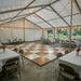 Tented event space with tables, chairs, and string lights. Natural White Dance Floor set up. 