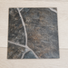 Close-up top view of a sample piece of Flagstone rolled vinyl flooring, featuring a dark gray and charcoal stone tile pattern with realistic light gray grout lines, displayed on a light oak wood grain background to show texture and thickness.
