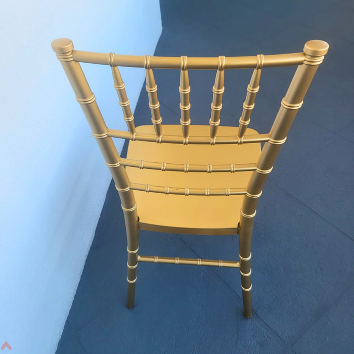 Rear high-angle view of a gold resin Chiavari chair, showing the textured bamboo-style backrest spindles and seat surface from behind against a blue backdrop