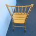 Rear high-angle view of a gold resin Chiavari chair, showing the textured bamboo-style backrest spindles and seat surface from behind against a blue backdrop