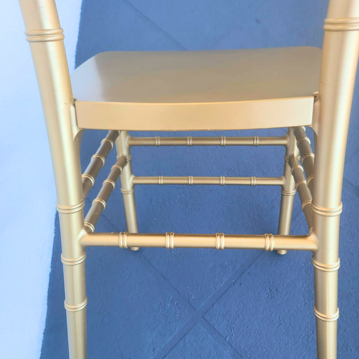 Close-up of the lower frame and legs of a gold resin Chiavari chair, showing the bamboo-style joints and supportive crossbar ring, set against a blue floor background