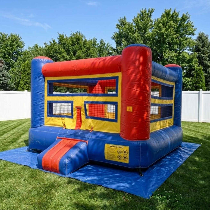 Beyond Tent Knockout Zone 15ft Commercial Boxing Bounce House, red blue and yellow boxing ring themed bounce house set up in a backyard with a white vinyl fence and mature trees