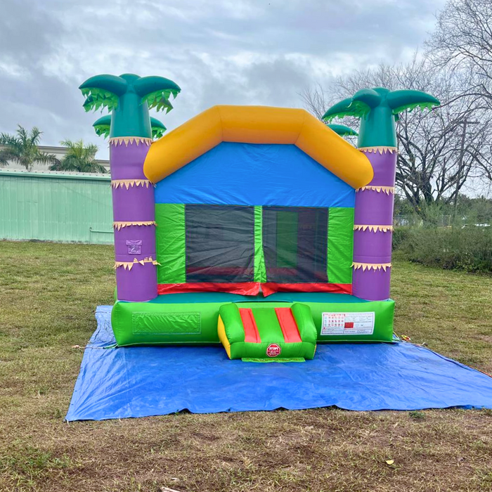 Beyond Tent Lightweight Palm Tree Bouncer set up on a blue tarp on grass, cloudy sky with an industrial building and trees in the background