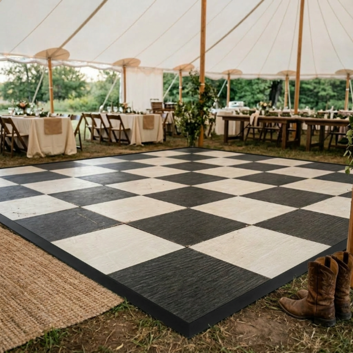 Beyond Tent Natural Black & White Checkered Portable Dance Floor w/ Edging installed under a sailcloth tent at a wedding reception, surrounded by wood folding chairs and a woven area rug