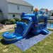 Ocean Shark Bounce House Combo set up on a grassy backyard lawn in front of a house. The slide has a shark-themed design with a blue water pool, clear slide panels, and a bouncy castle with windows and a shark decoration on the side.