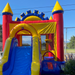 Side angle of the Rainbow Play Wet & Dry inflatable combo showing the heavy-duty yellow entrance ramp, secure mesh safety netting on the bounce house walls, and the high-walled blue slide exit. A commercial-grade 18oz PVC vinyl unit set up outdoors.