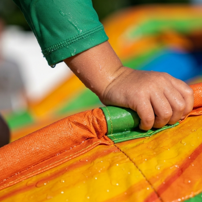 Child's hand holding onto a colorful inflatable slide with a blurred background