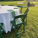 Resin Folding Chair Green - 1100 lb Capacity tablecloth-covered table with green folding chairs on a grassy outdoor lawn, with a golf cart visible in the background.
