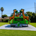 Beyond Tent Rumble Bounce House 13x13 with Blower set up on a green lawn with a palm tree in the background, giraffe toppers and jungle animal mural, sunny day