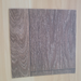 Rustic Oak vinyl flooring plank sample laid diagonally on a light natural wood surface, showing the brown wood-look grain pattern from an angle