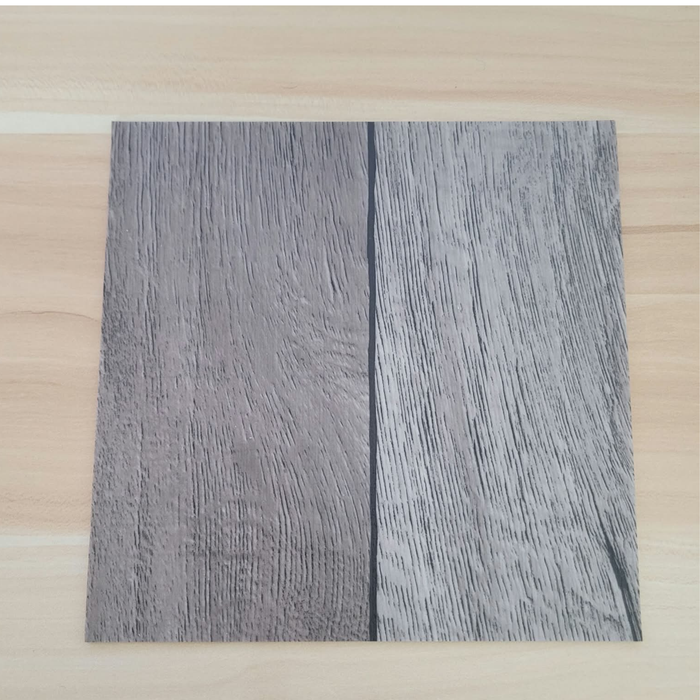 Beyond Tent Silver Oak commercial-grade vinyl flooring tile sample placed on a light wood-tone surface for color comparison