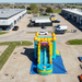 Aerial view of a commercial-grade Solar Dual Lane inflatable combo water slide with castle turrets and a sun graphic, fully inflated on a blue protective ground tarp in an outdoor paved lot.