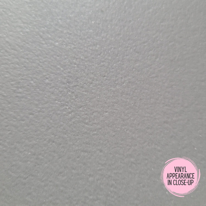 A close-up texture of the solid grey roller vinyl material with a subtle pebbled or brushed finish, featuring a pink circular badge in the bottom right corner that reads 'VINYL APPEARANCE IN CLOSE-UP'.