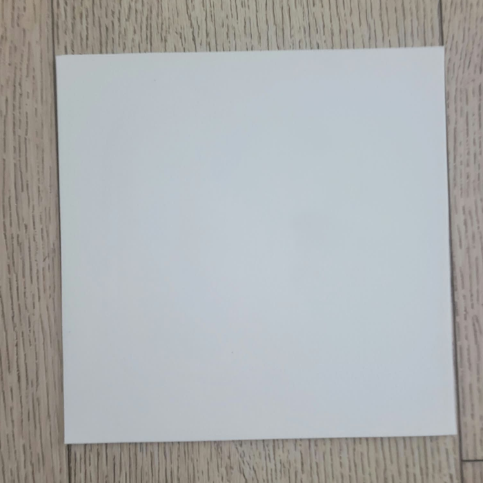 Matte White Rolled Vinyl Flooring sample swatch laid flat on a light oak wood plank floor, straight-on angle