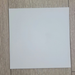 Matte White Rolled Vinyl Flooring sample swatch laid flat on a light oak wood plank floor, straight-on angle
