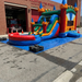 Twin Tower Dash commercial bounce house combo – angle view highlighting the dual castle towers, vibrant primary color scheme, and bounce chamber with safety mesh netting on all sides