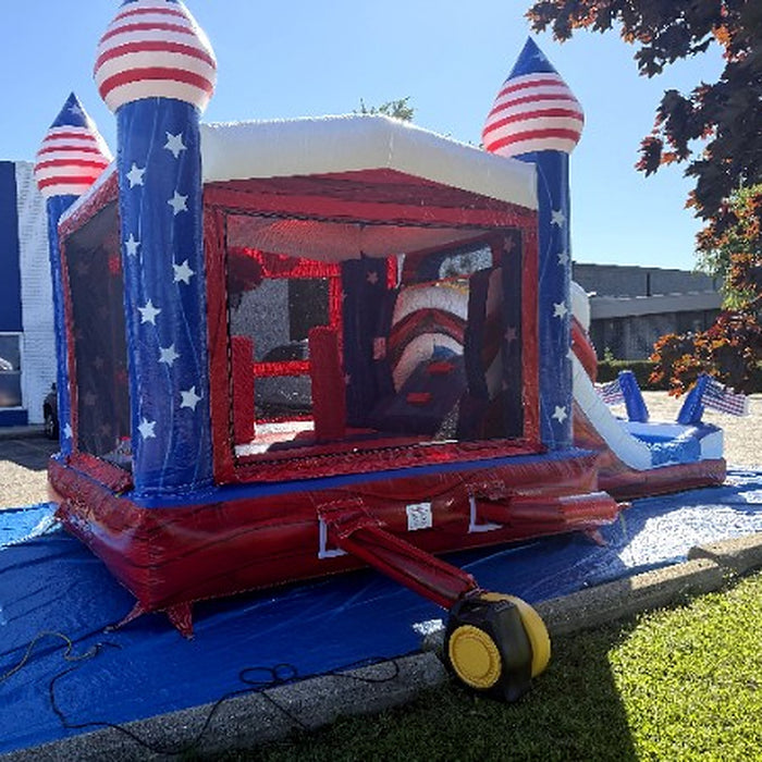 Side view of the American Titan Wet and Dry Combo bounce house, mesh windows, star-covered blue towers with striped dome tops, red marble base and the included yellow commercial blower