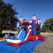 American Titan Wet and Dry Combo set up outdoors on a blue tarp, blue slide with white rails into a splash pool with two American flags, red marble vinyl and striped dome towers