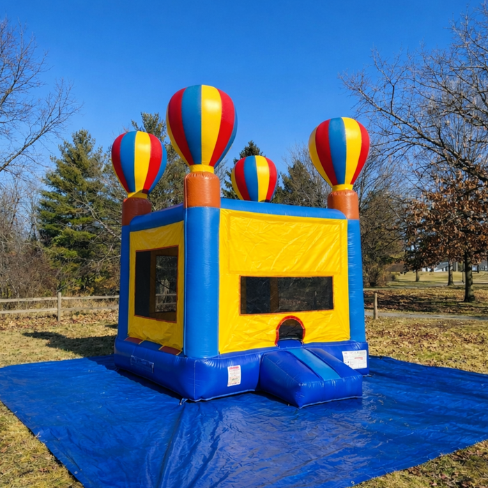 Beyond Tent 13x13 Celebration Bouncer with 18oz commercial PVC vinyl and hot air balloon corner pillars, set up on a manicured grass lawn with a professional wood fence and tree background.