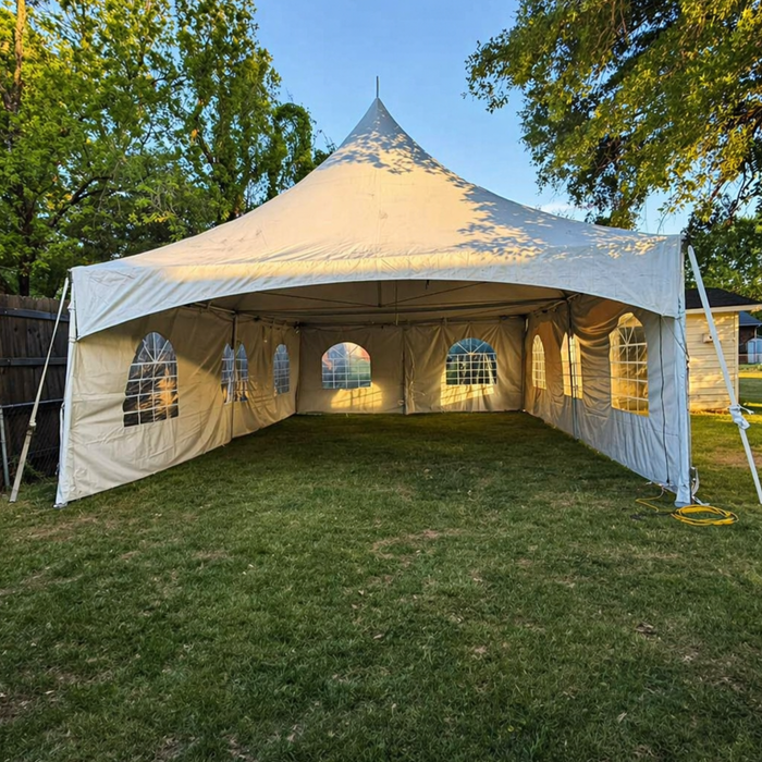 Beyond Tent 20x20 High Peak Frame Tent featuring a high-tension center mast and cathedral window sidewalls, professionally installed on a grass lawn with a wooden fence and tree line