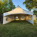 Beyond Tent 20x20 High Peak Frame Tent featuring a high-tension center mast and cathedral window sidewalls, professionally installed on a grass lawn with a wooden fence and tree line