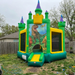 Side view of the Beyond Tent Dino-Dome commercial bounce house featuring high-definition T-Rex and Triceratops printed graphics, purple castle spires, and a yellow mesh safety entrance in a backyard setting.