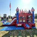 American Titan Wet and Dry Combo set up on a blue tarp in a grassy park with a flagpole, front entrance ramp, USA letters, mesh bounce windows, slide and splash pool connected to a hose