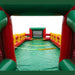 Interior view of a commercial inflatable human foosball arena showing the green vinyl playing floor, red side walls, yellow safety ropes, and a built-in soccer goal net.