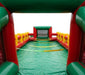 Interior view of a commercial inflatable human foosball arena showing the green vinyl playing floor, red side walls, yellow safety ropes, and a built-in soccer goal net.